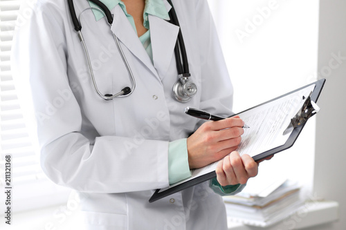 Female doctor filling up medical form on clipboard closeup.  Healthcare, insurance and medicine concept photo