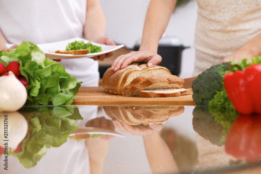 Closeup of human hands cooking in kitchen. Mother and daughter or two female friends cutting bread. Healthy meal, vegetarian food and lifestyle concept Closeup of human hands cooking in kitchen. Mother and daughter or two female friends cutting bread. Healthy meal, vegetarian food and lifestyle concept