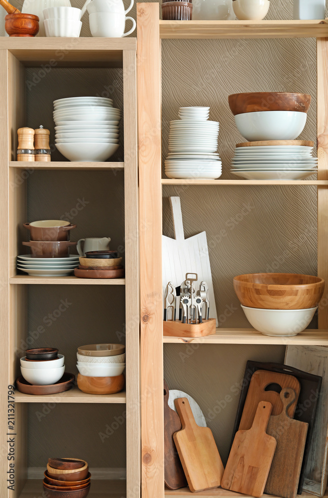 Storage stand with ceramic and wooden kitchenware on color background