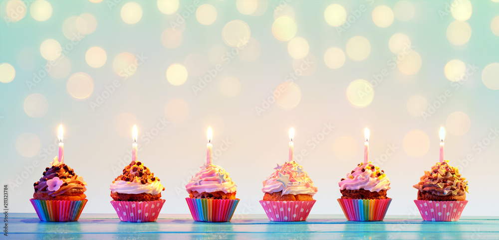 Row Of Colorful Cupcake With Candles And Bokeh Lights - obrazy, fototapety, plakaty 