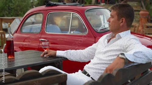 Handsome middle-aged man drinking wine with his vintage car in background