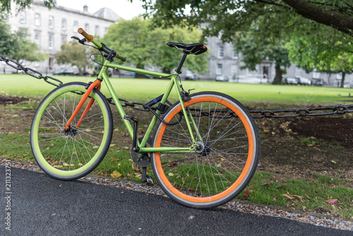 Photography Colourful, green and orange bicycle locked to a chain-link fence in the grounds of the university in Dublin, Republic of Ireland