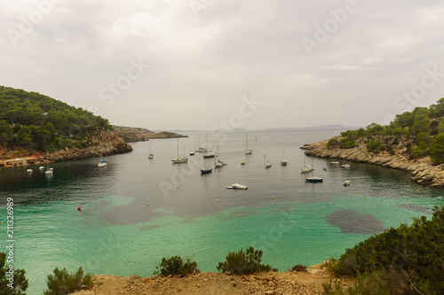 Benirras beach, Ibiza, Spain - 27 August, 2017: Sailing boats on Cala d'Hort bay with beautiful azure blue sea water, Ibiza island, Spain photo