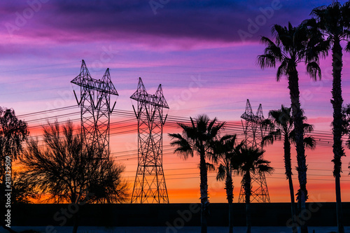 Silhouette of high voltage lines and transmission towers thru the desert at sunset.