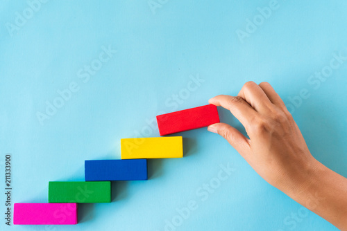 Concept of building success foundation. Women hand put red wooden block on colorful wooden blocks in the shape of a staircase photo