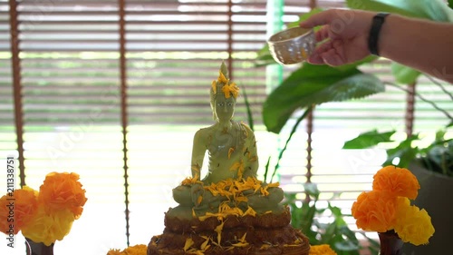 Buddhist Songkran. The Thai new year. Mens hand pours a Buddha statue with water and jasmine petals photo