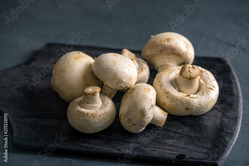 White champignons on the dark kitchen table. Cooking delicious dishes with mushrooms