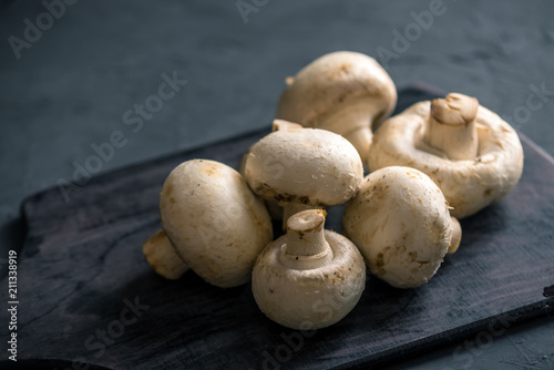 White champignons on the dark kitchen table. Cooking delicious dishes with mushrooms