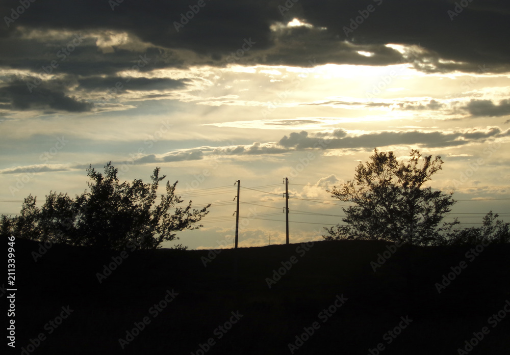 Power lines at sunset. A silhouette of high voltage power lines. Pylons and transmission power line in sunset. Hill. Trees