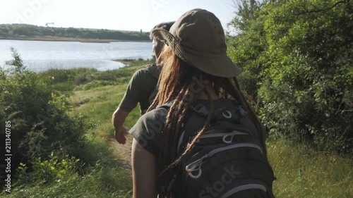 Couple of backpackers travel near river in summer sunny day 