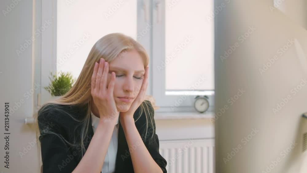 Upset woman sitting at workplace. Blond sad female in elegant clothes clutching head after failure or bad news sitting in light office at desk with computer. Upset woman sitting at workplace. Blond sad female in elegant clothes clutching head after failure or bad news sitting in light office at desk with computer.