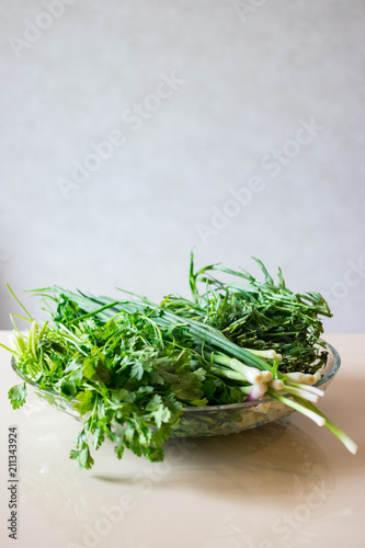 A bunch of greens and herbs. Green onion sprouts, cilantro, tarragon in glass bowl.