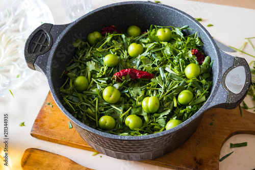 Preparation or cooking of chakapuli in cauldron pan. Ingredients: lamb meat, green tkemali sour plum, onion sprouts, cilantro, tarragon leaves. Georgian traditional stew photo