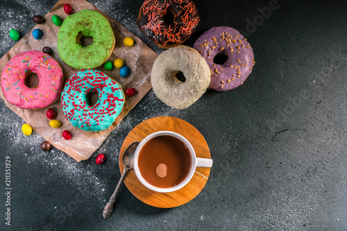 Donuts with colorful icing and hot cocoa on a dark background. Top view