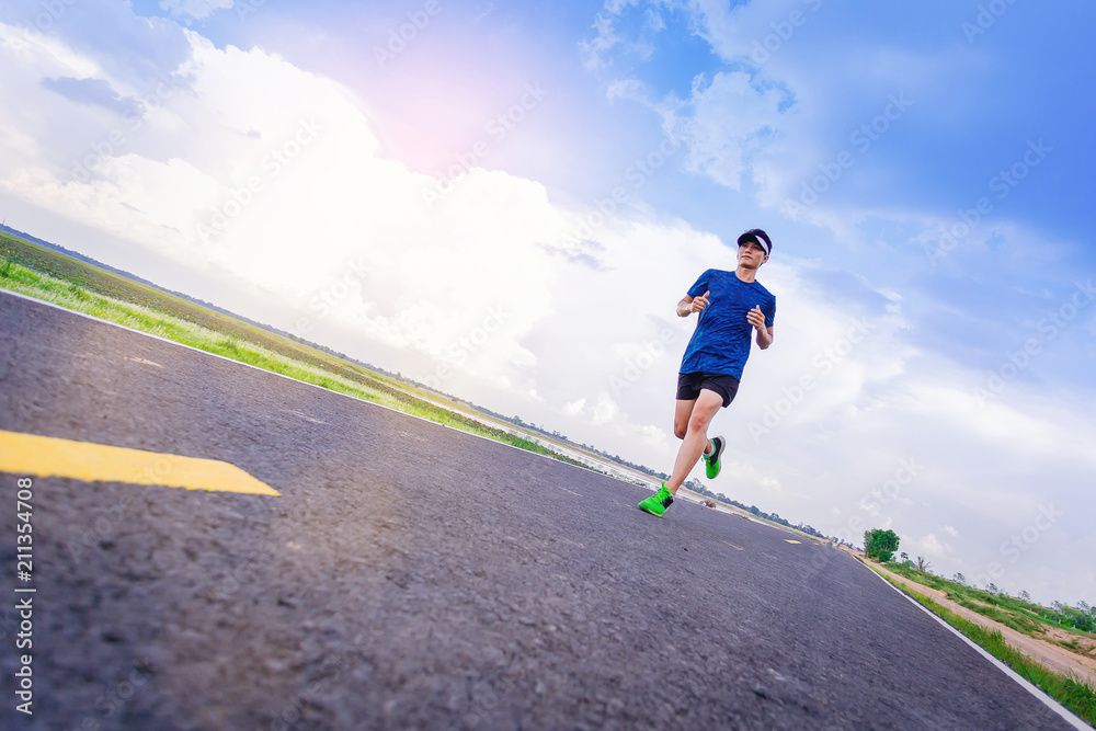 Young man jogging along the road. with cloudy sky as background