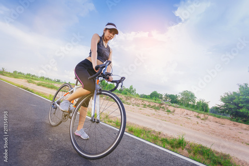 Sporty girl cyclist riding sprint bicycle along the bike lane with cloudy sky as background