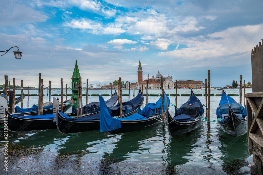 Gondolas moored by Saint Mark square with San Giorgio di Maggiore church on blurry background in Venice, Italy