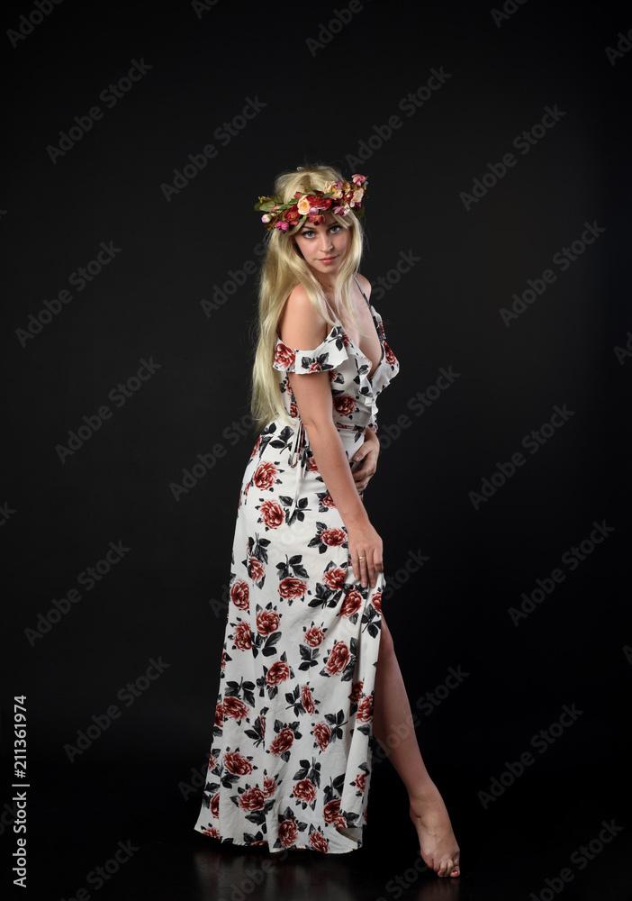 full length portrait of blonde girl wearing floral dress and a flower crown. standing pose against a black studio background. full length portrait of blonde girl wearing floral dress and a flower crown. standing pose against a black studio background.