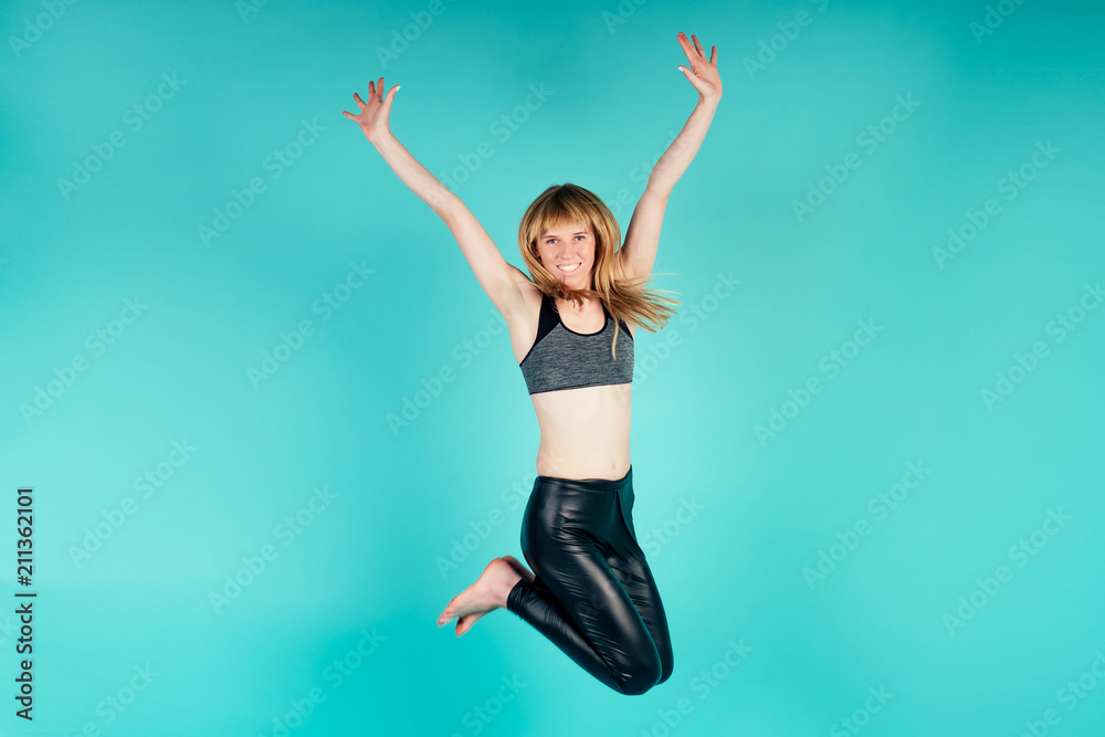Asanas coach young and active blonde woman jumping in studio on blue background studio shot