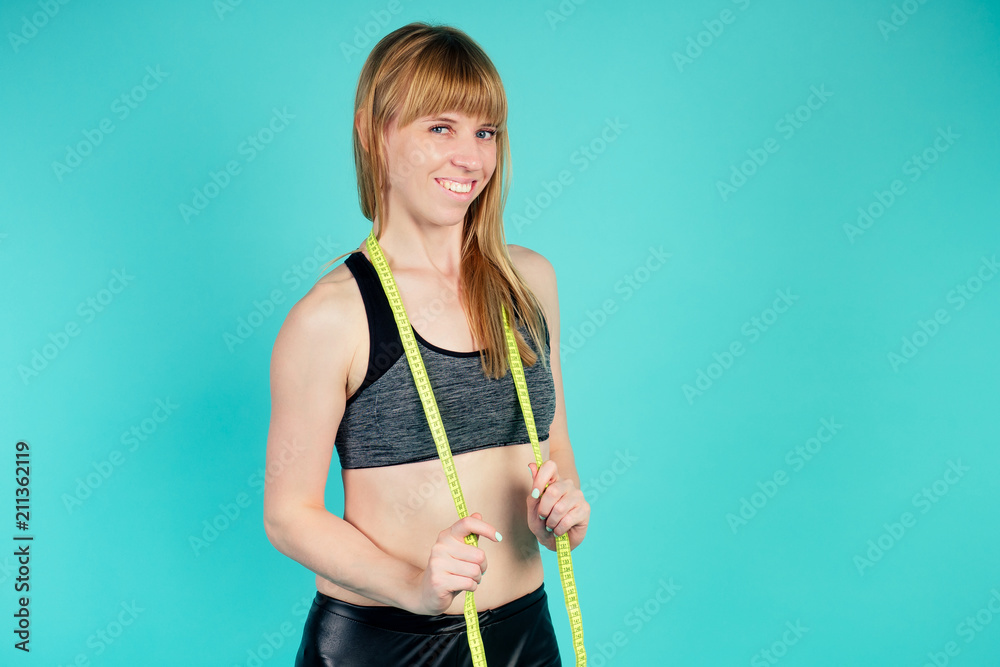 young and active blonde woman posing with a measuring tape in studio on blue background