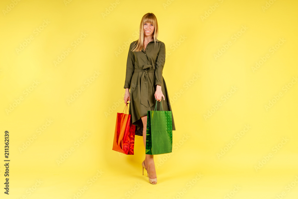 young and active blonde woman holds a lot of shopping bags in studio on yellow background young and active blonde woman holds a lot of shopping bags in studio on yellow background