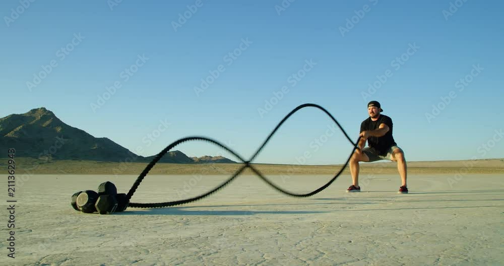 Slow motion: Athletic man doing crossfit battle rope workout outside in desert 