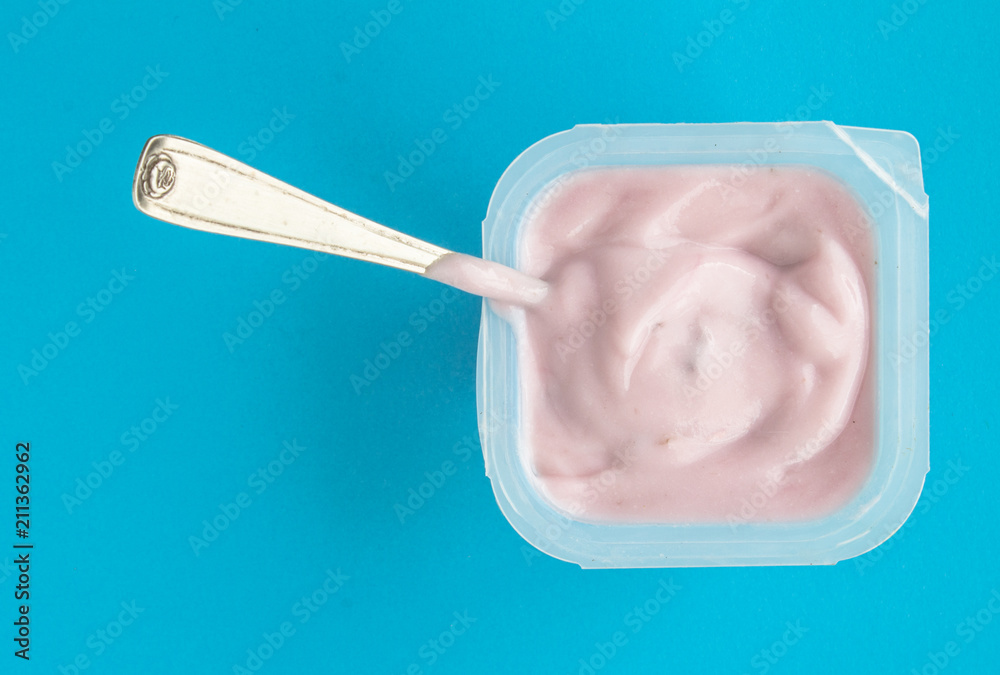 Yogurt in plastic cup close up - Pink yoghurt on blue background with small silver spoon Yogurt in plastic cup close up - Pink yoghurt on blue background with small silver spoon