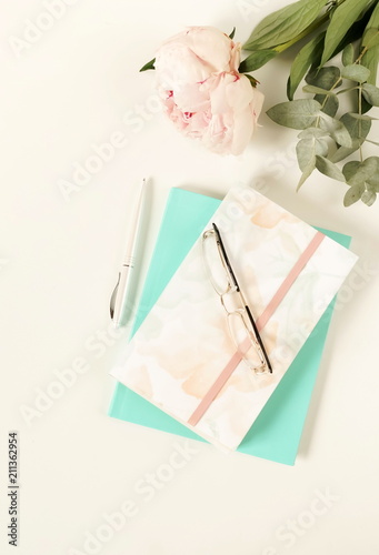 Flat lay women's office desk. Female workspace with flowers peonies,  accessories, notebook, glasses on white background. Top view feminine background.Copy space