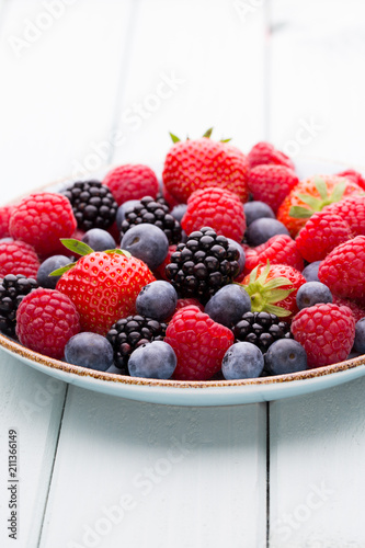 Fresh berry salad on blue dishes. Vintage wooden background.