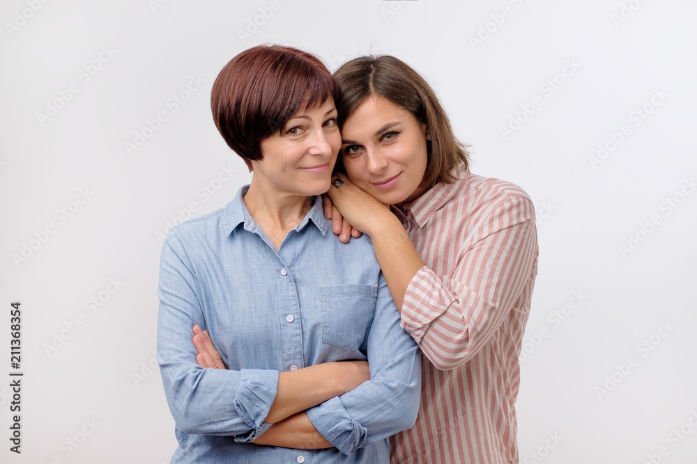 Beautiful maturesenior mom and her adult daughter are hugging, looking at camera and smiling. Good relationships between generations. Beautiful maturesenior mom and her adult daughter are hugging, looking at camera and smiling. Good relationships between generations.