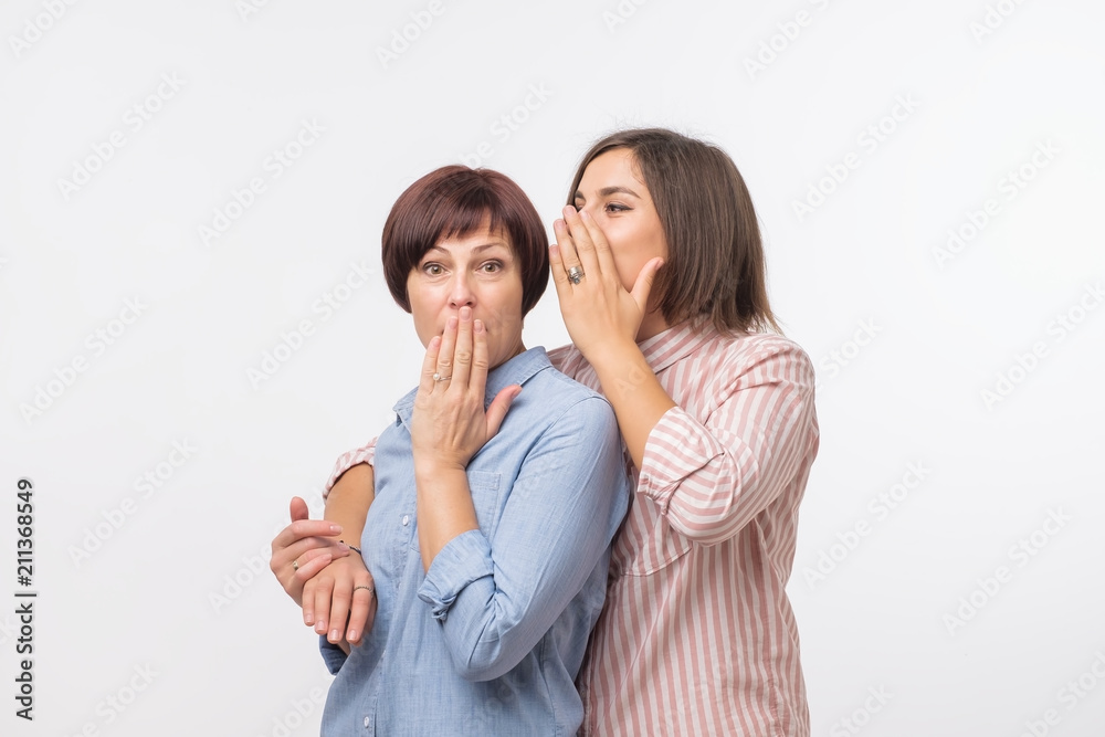 Women mother and daughter gossiping and telling a secret isolated over gray background Women mother and daughter gossiping and telling a secret isolated over gray background
