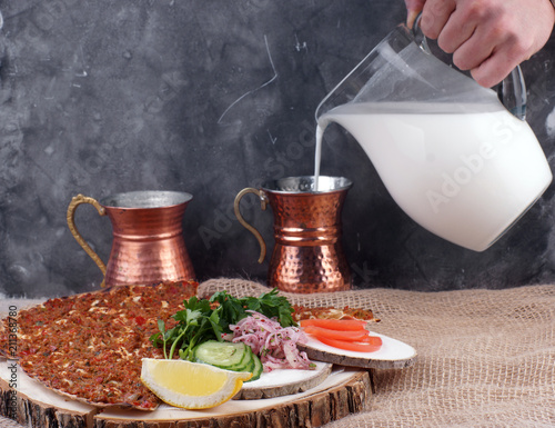 Lunch with Turkish tortilla Lagmajun, a man's hand pours a Turkish national drink ayran in special dishes photo