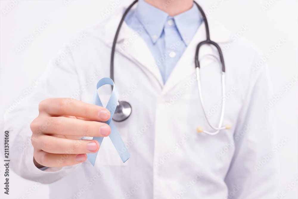 Oncological disease concept. Doctor wearing white coat and stethoscope holding blue ribbon as a symbol of prostate cancer. Oncological disease concept. Doctor wearing white coat and stethoscope holding blue ribbon as a symbol of prostate cancer.