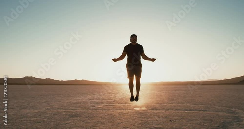 Slow motion: Athletic man working out outside in desert at sunset jumping rope 