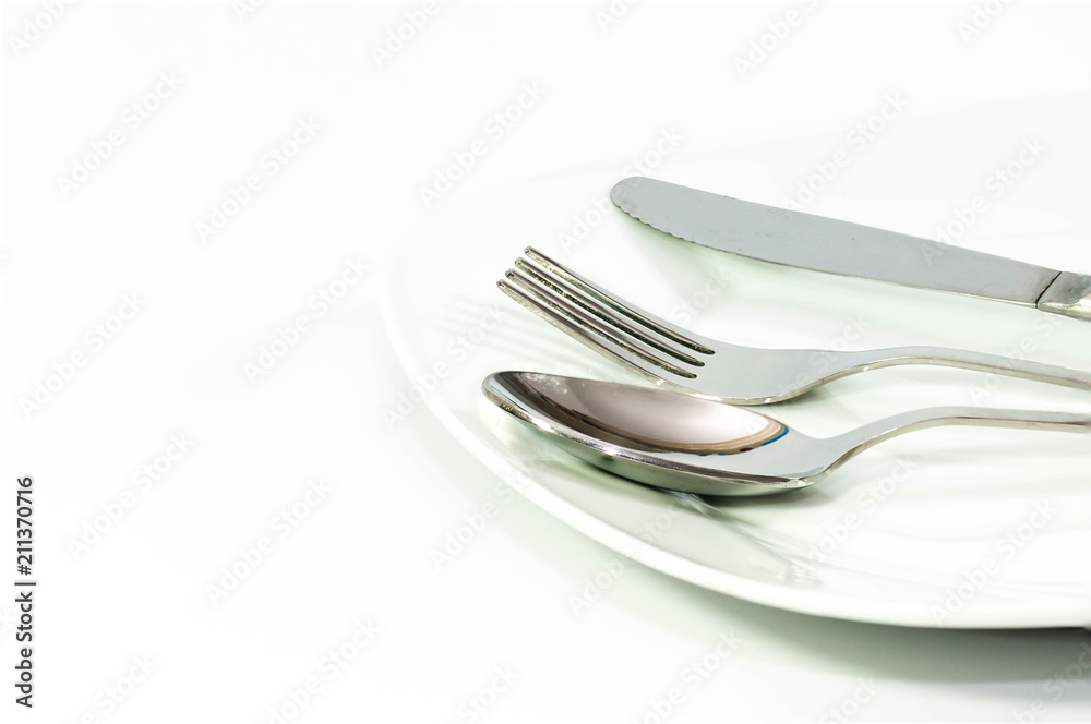 Shiny stainless fork, knife and spoon on white plate on white background. Shiny stainless fork, knife and spoon on white plate on white background.