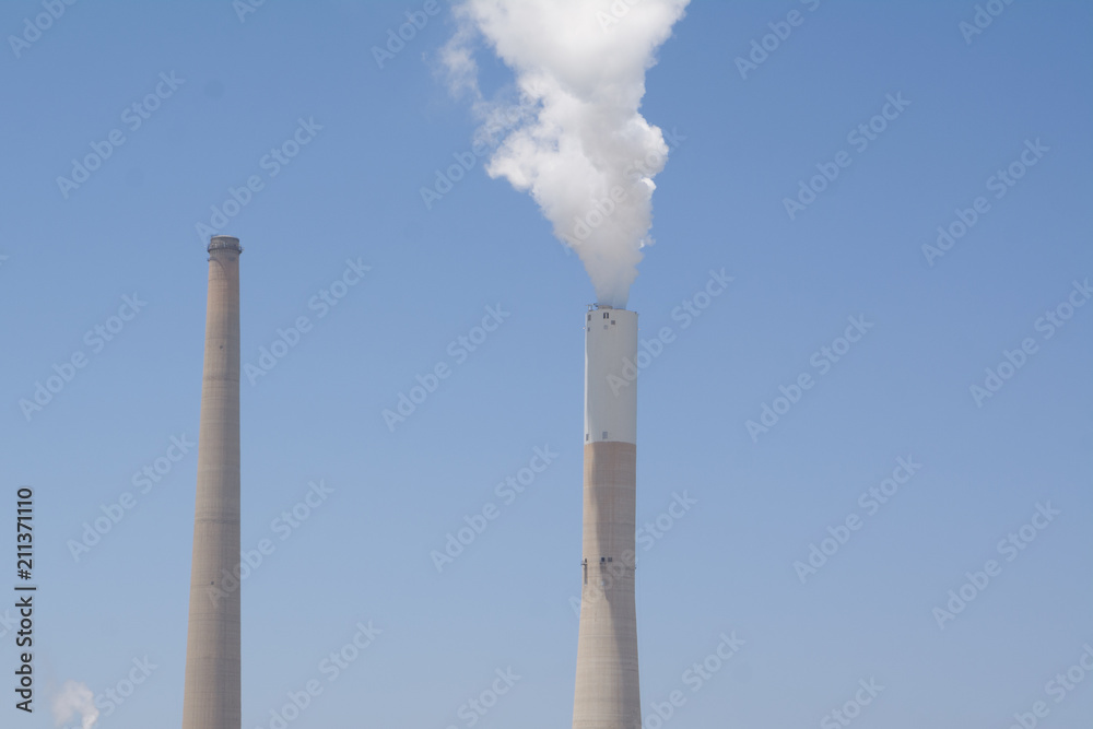 White smoke rises from the striped pipe into the blue cloudless sky on a bright, sunny day. Coal and Gas fired power station - Aerial view including a Flue-Gas chimney