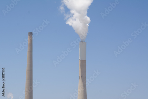 White smoke rises from the striped pipe into the blue cloudless sky on a bright, sunny day. Coal and Gas fired power station - Aerial view including a Flue-Gas chimney