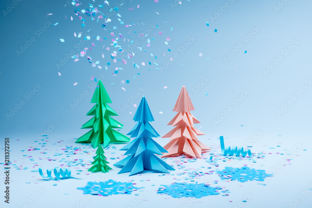Multicolored paper fir trees with blue snowflakes and falling confetti. Christmas concept. Artificial winter miniature.