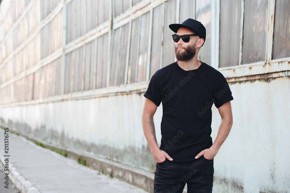 Hipster handsome male model with beard wearing black blank t-shirt with space for your logo or design in casual urban style - obrazy, fototapety, plakaty 
