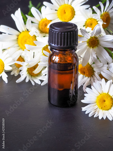 Chamomile oil bottle with flowers on black  background

