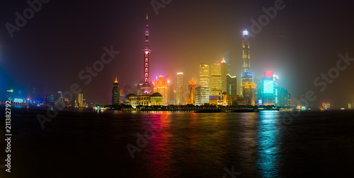 Shanghai skyline glowing in a misty night, reflecting in Huangpu river