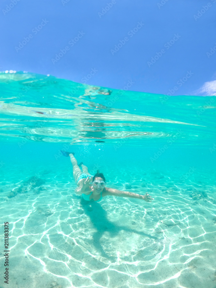 HALF UNDERWATER: Active woman on holiday snorkels in ocean and gives the ok sign