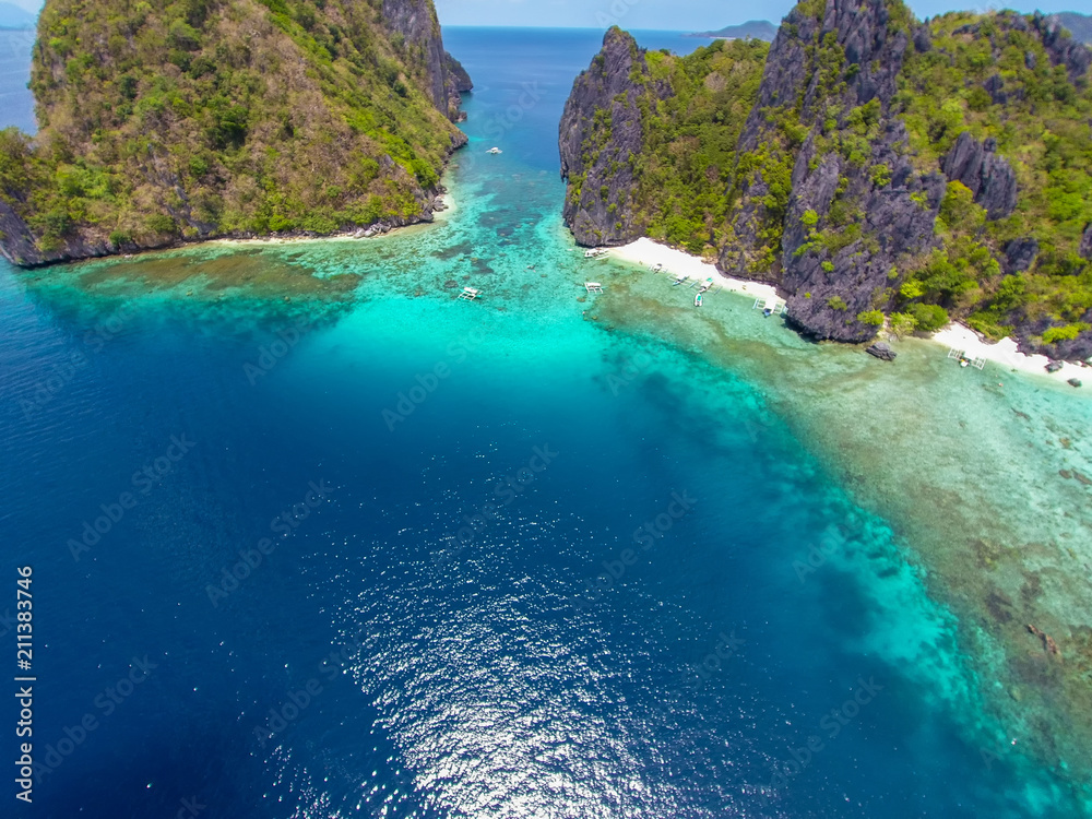 The azure blue sea. Top view of a tropical island with palm trees and blue clear water. Aerial view of a white sand beach and boats over a coral reef. The island of Palawan, Philippines.