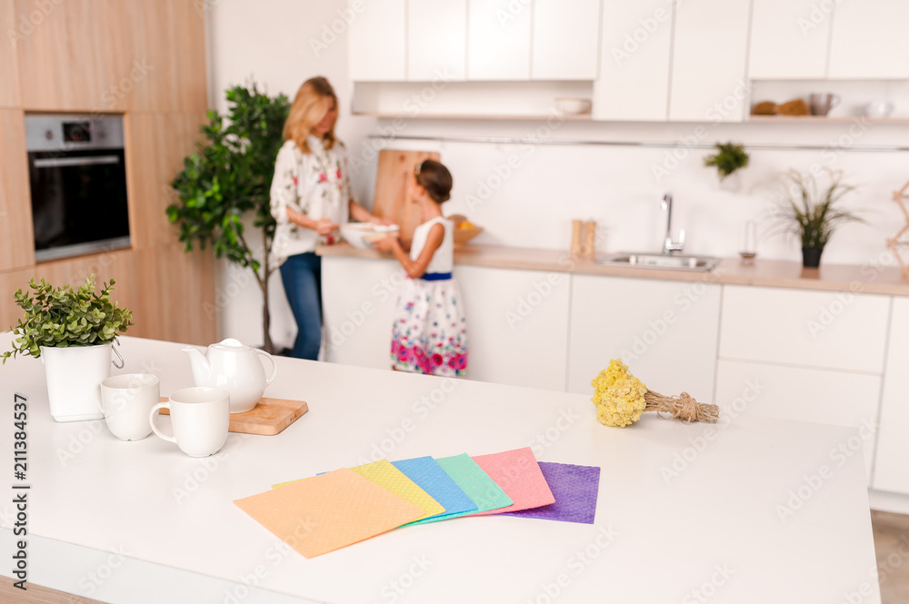 Daughter and mother blur on the back side. On the table in the kitchen lie rags for cleaning of different colors Daughter and mother blur on the back side. On the table in the kitchen lie rags for cleaning of different colors