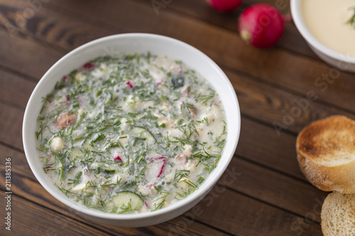 Summer yoghurt cold soup with radish, cucumber, and dill on wooden table. Okroshka.