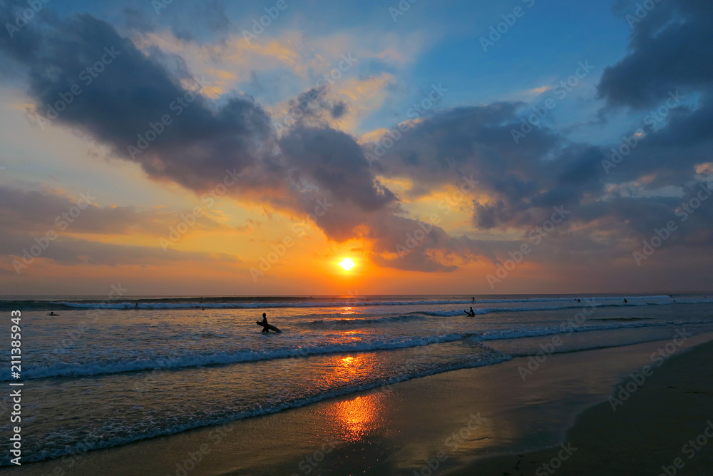 Amazing Kuta beach sunset with ocean waves, surfers and reflection in wet sand, Bali, Indonesia