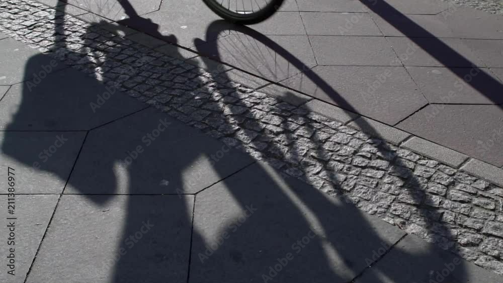 Slow Motion Shot Of Multiple Bicycle Riders In Shadow Cycling On A Bicycle Lane On The Sidewalk In Berlin. Slow Motion Shot Of Multiple Bicycle Riders In Shadow Cycling On A Bicycle Lane On The Sidewalk In Berlin.