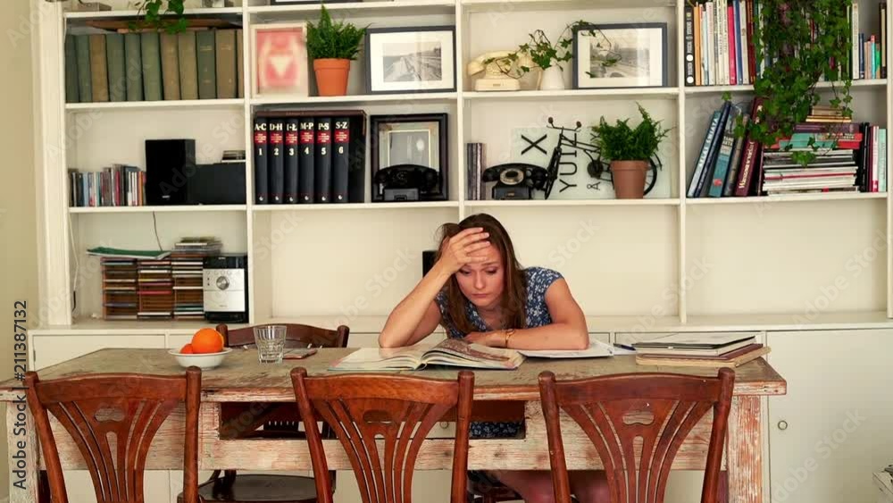 Sad, overwhelmed student sitting with books by table at home
