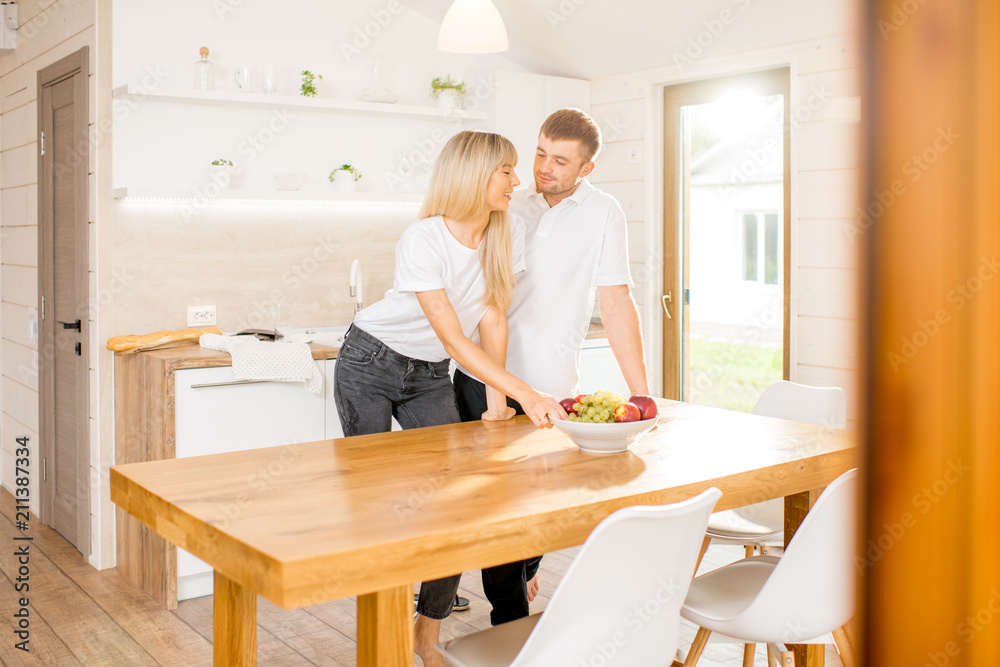 Young couple standing together at the dining room of the modern wooden country house. View inside through the window Young couple standing together at the dining room of the modern wooden country house. View inside through the window