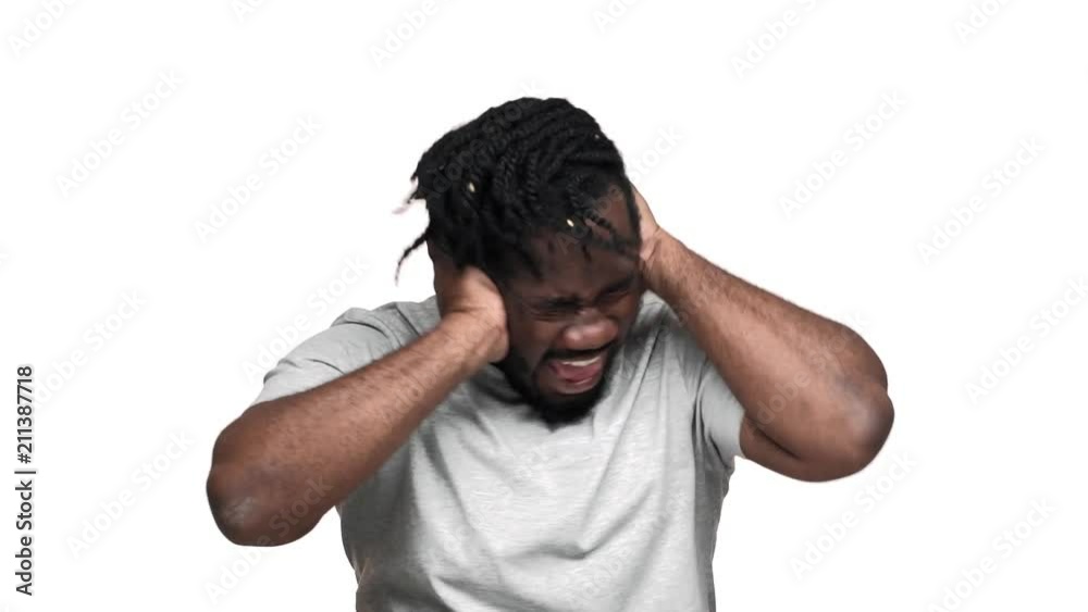 Portrait of frightened dark skinned guy with afro pigtails covering ears while screaming due to annoying noise, isolated over white background slow motion. Concept of emotions Portrait of frightened dark skinned guy with afro pigtails covering ears while screaming due to annoying noise, isolated over white background slow motion. Concept of emotions